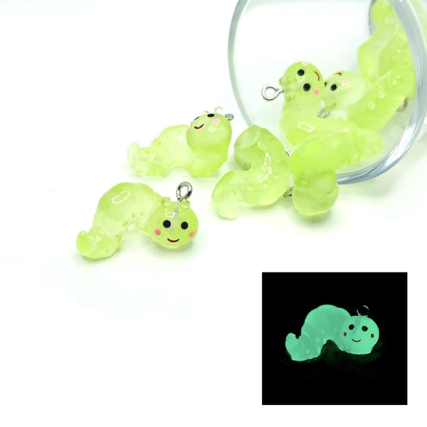 Glowing green caterpillar-shaped charms with a clear container on a white background.