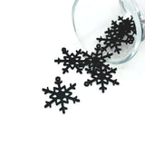Black snowflake charm with symmetrical, intricate cut-out design, approx. 22×26 mm, shown against a white background.
