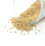 Glass container of light brown beads spilling onto a white surface