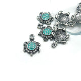 Silver turtle charms with turquoise centers on a white background