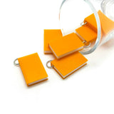 Set of small orange book charms with metal rings on a white background