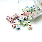 Colorful alphabet beads spilling out of a clear container on a white background