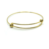 A slim, gold-tone expandable wire bangle with overlapping ends, shown flat on a white background to highlight its reflective surface and sleek profile.