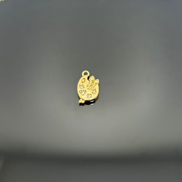 A shiny gold-tone miniature paint palette charm with brush detail, measuring approximately 14 × 8 mm, shown on a white background.