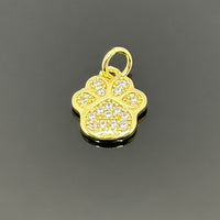 A small gold-plated paw print charm, approximately 16×11 mm, covered in micro pave cubic zirconia, displayed on a black background.