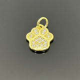 A small gold-plated paw print charm, approximately 16×11 mm, covered in micro pave cubic zirconia, displayed on a black background.