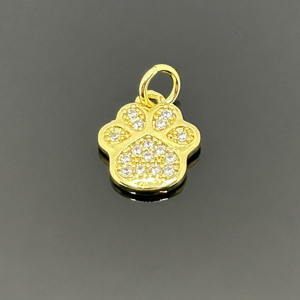 A small gold-plated paw print charm, approximately 16×11 mm, covered in micro pave cubic zirconia, displayed on a black background.