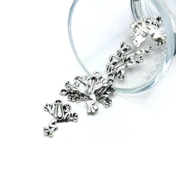 An antique silver-toned frog charm, approximately 17 × 22 mm, with raised detailing that resembles a playful frog, shown against a white background.