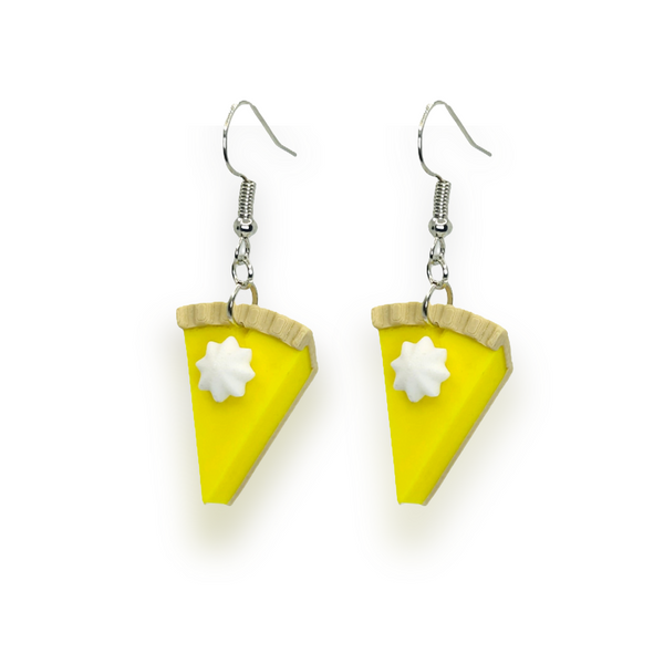 Pair of dangle earrings each featuring a lemon meringue pie slice charm topped with whipped cream and attached to metal ear wires, displayed on a white background