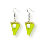 Pair of miniature key lime pie slice earrings with green filling and whipped cream details, displayed on a white background.